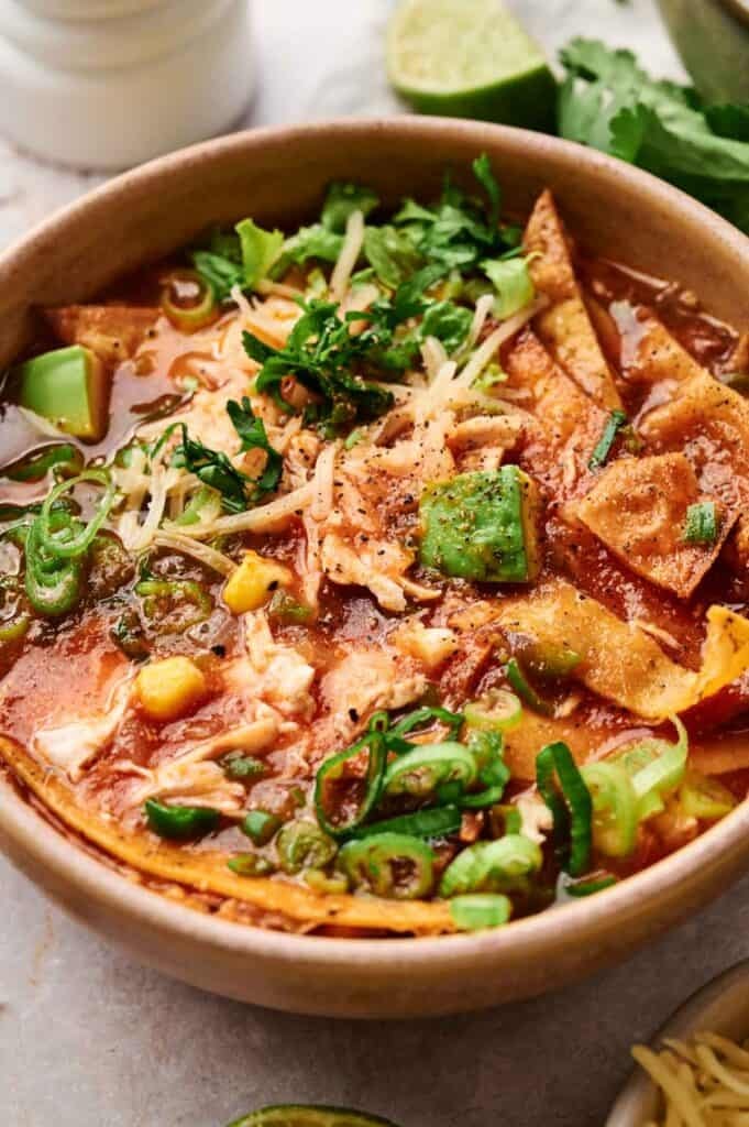 image of tortilla soup in a bowl with lime wedges and basil