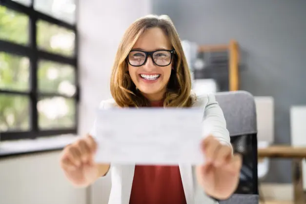 image of a woman in glasses smiling and presenting her paycheck
