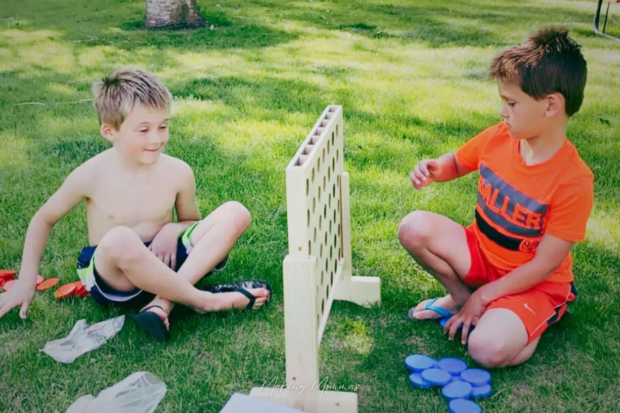 an image of two boys playing giant connect four out in the grass.