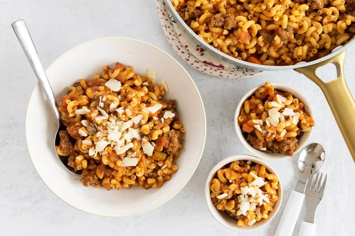 image of a bowl of pasta, with a skillet of pasta and two small bowls filled with hamburger pasta