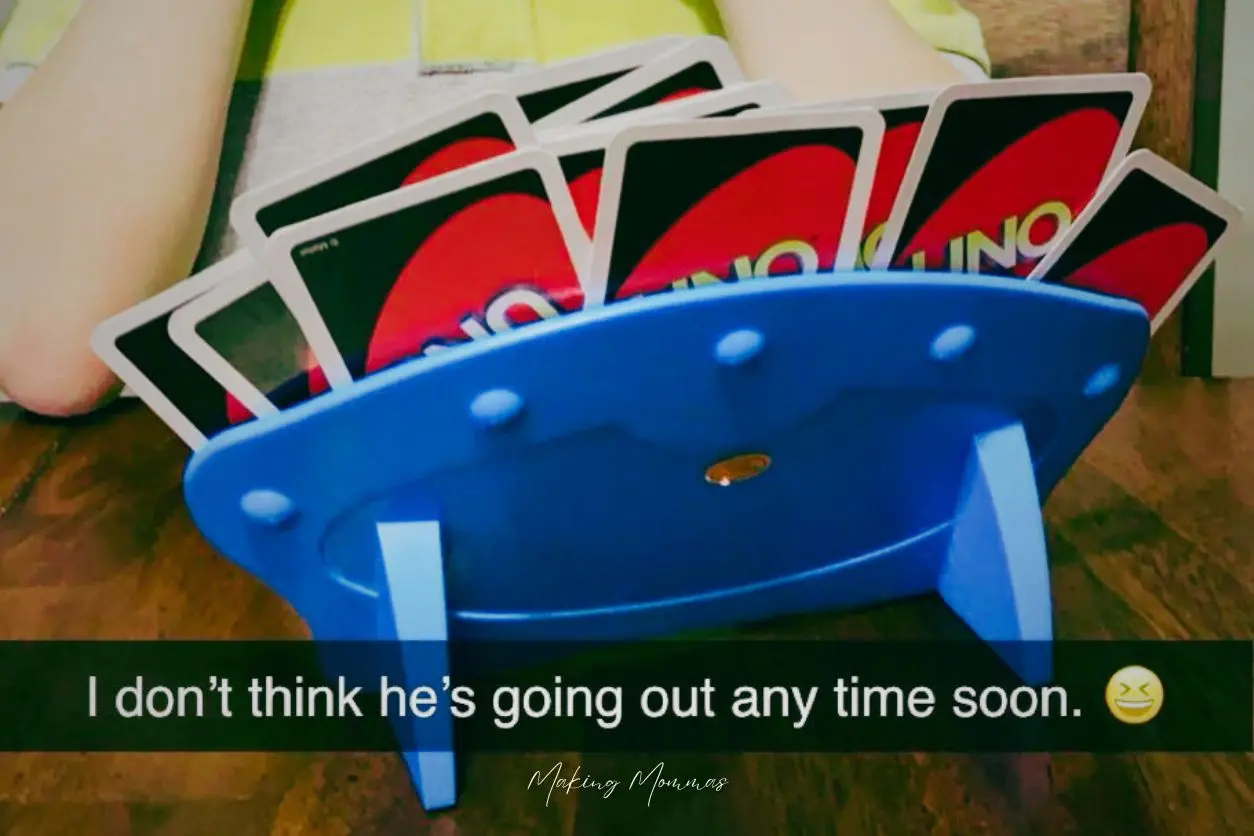 image of a card holder holding a lot of uno cards with a kid in the background and it reads, "I don't think he's going out any time soon."
