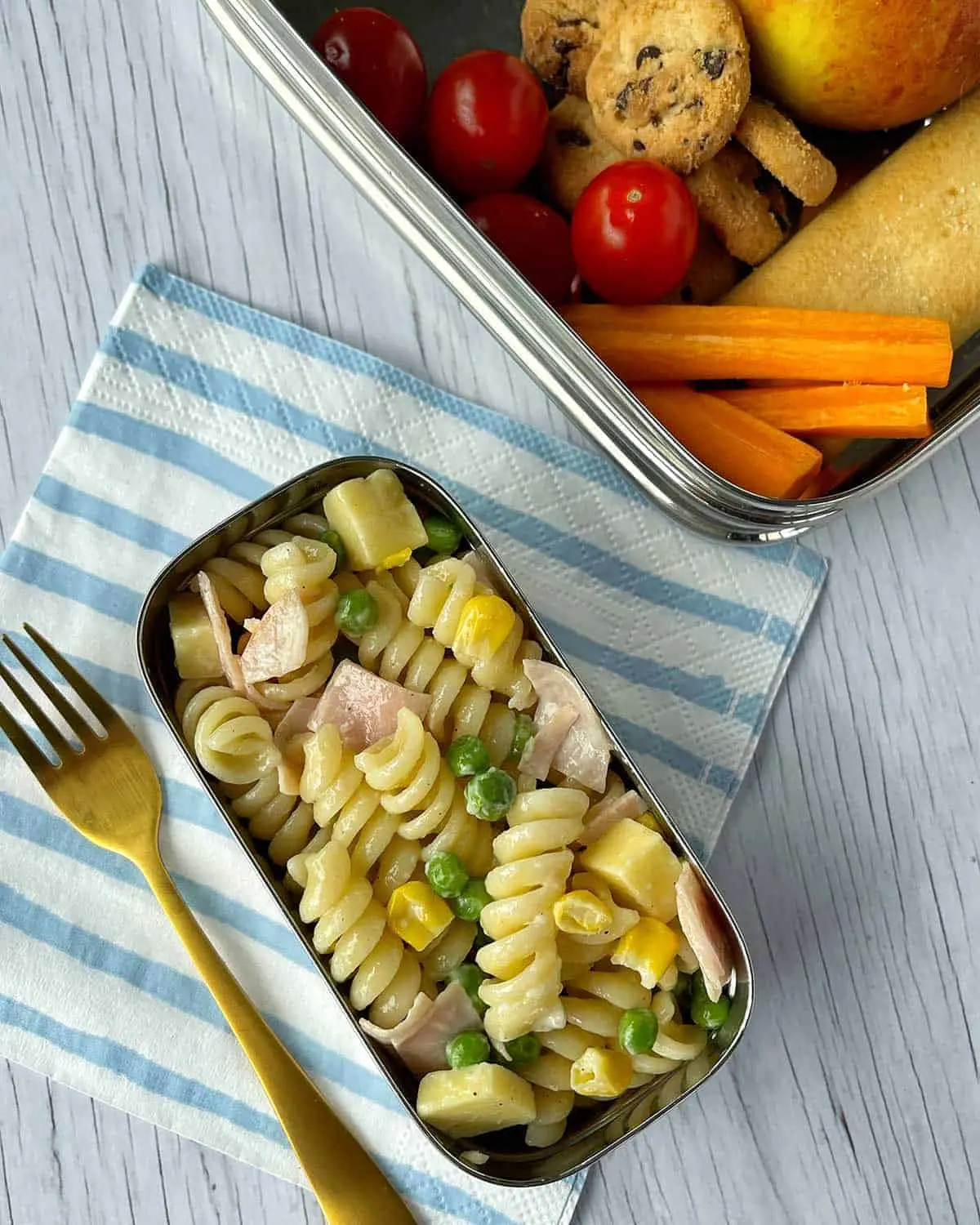 image of pasta salad in a lunch box tin, with a side of veggies, an apple, a breadstick, and cookies