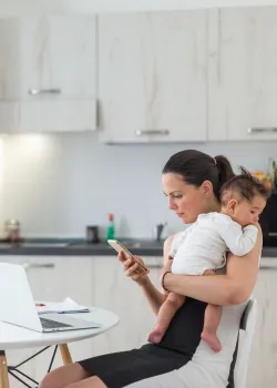 woman holding a baby in the kitchen looking at cell phone