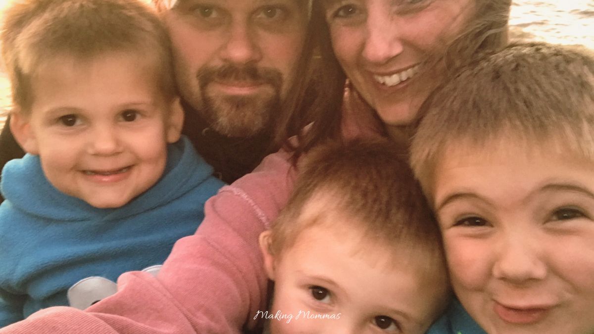 Close-up family selfie with smiling parents and children, wrapped in cozy clothing at sunset, capturing a joyful bonding moment.