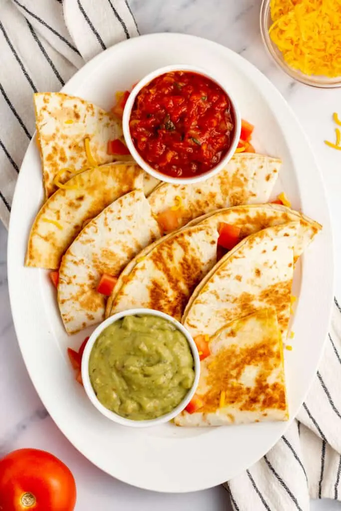 image of a cheese quesadilla cut into triangles on a plate with salsa and guac