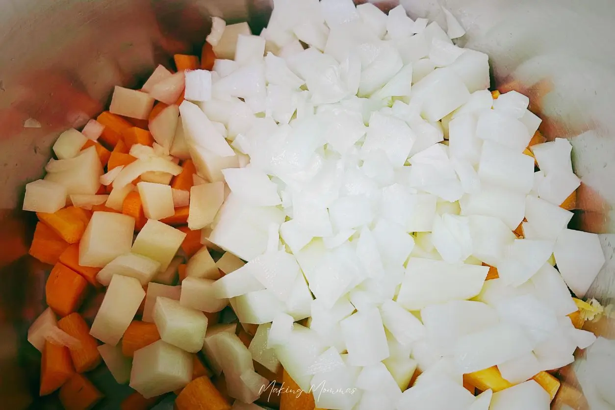 An image of chopped veggies, including carrots, onions, and potatoes, in a pot.