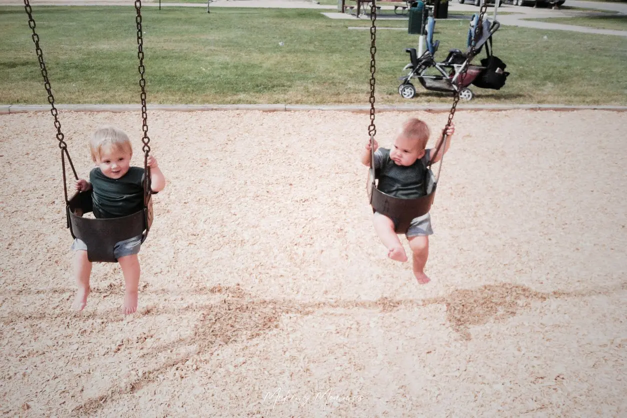 image of two twin toddlers swinging in baby swings at the park