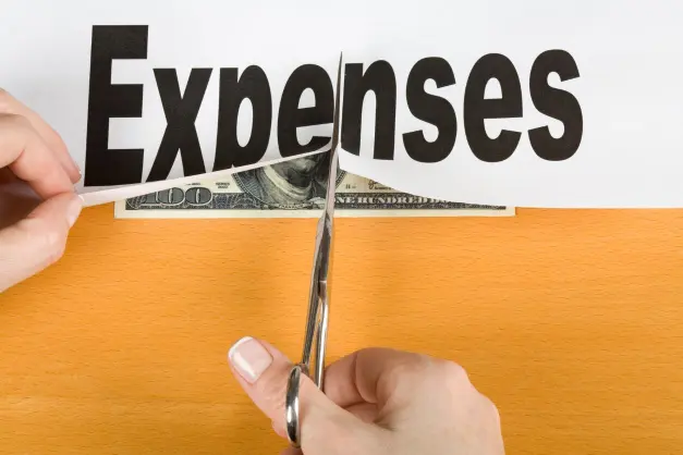 image of someone cutting the word "expenses" in half, with a hundred dollar bill peeking out from underneath