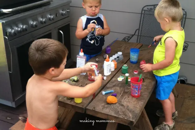 three boys playing painting rocks on a picnic table