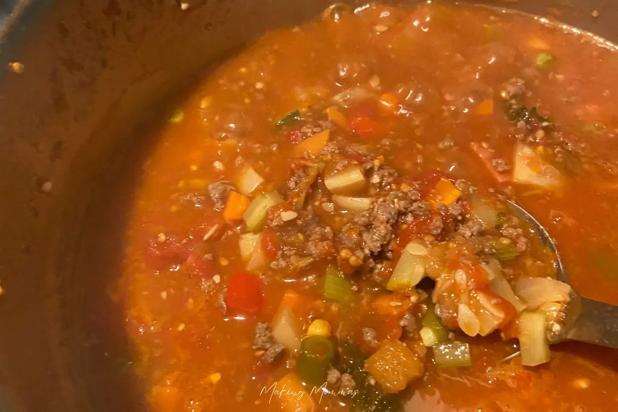 Image of a spoon stirring the hamburger vegetable soup in the soup kettle.