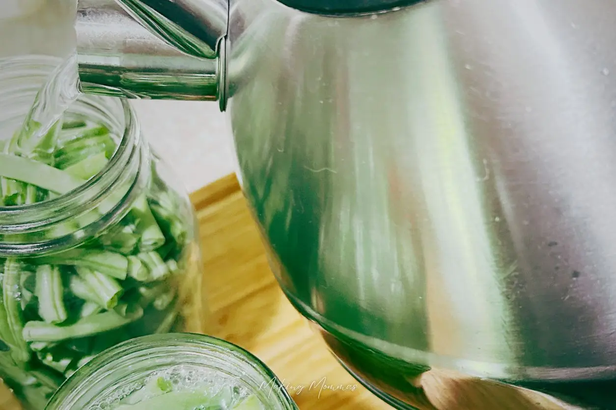 image of pouring water into a jar of packed green beans with a tea kettle