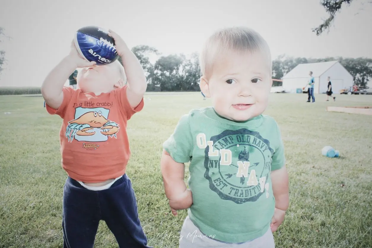 image of two toddlers playing outside. One has a football on his face. There are two older kids in the background.