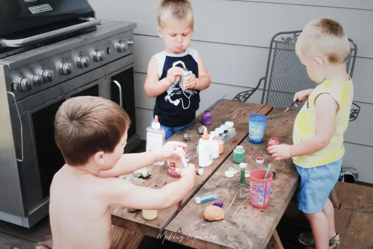 image of three little boys painting rocks on a tiny picnic table outside