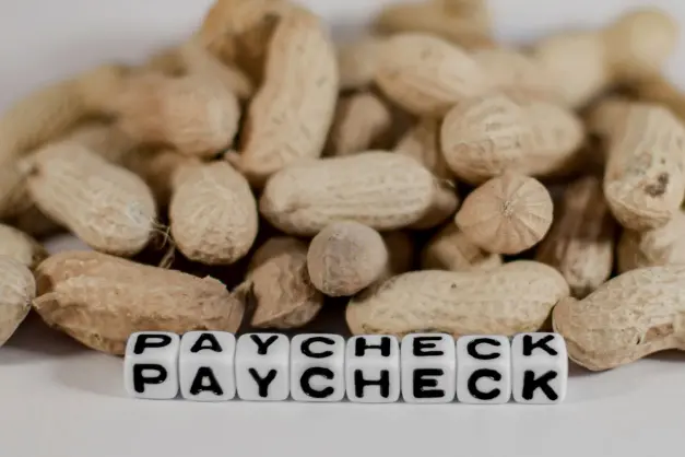 image of beads that spell out 'paycheck' in front of a pile of peanuts