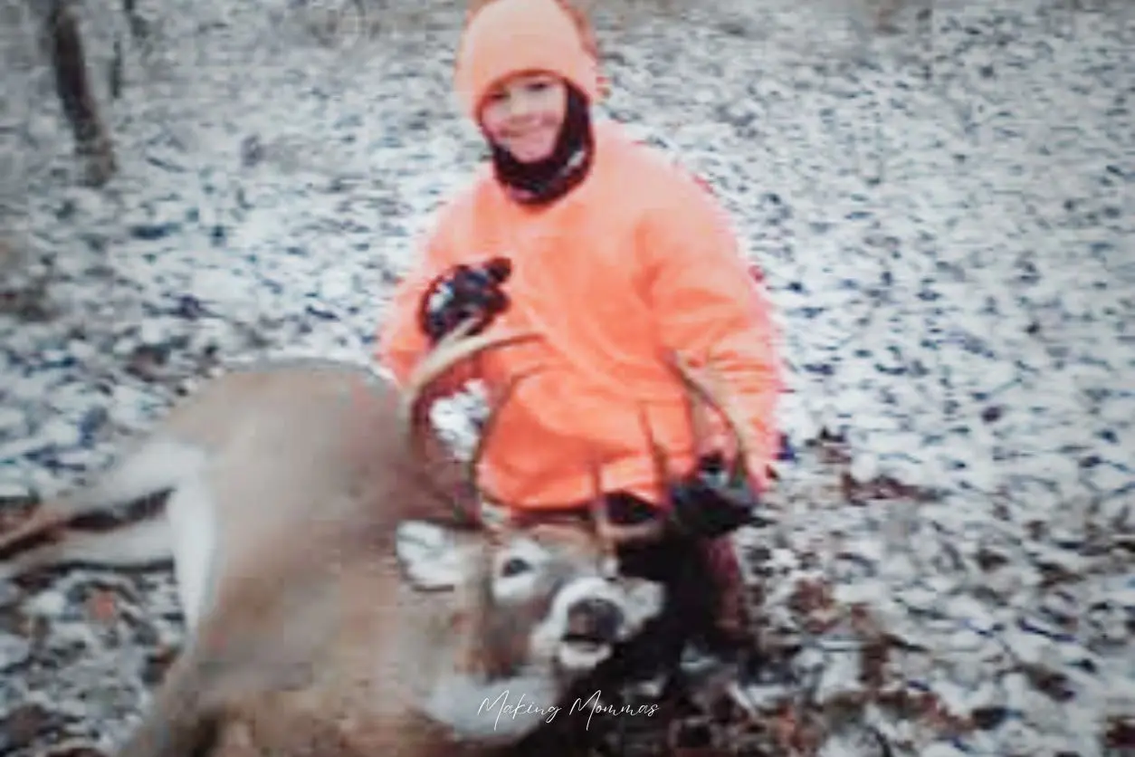 image of a boy in orange holding the antlers of a deer