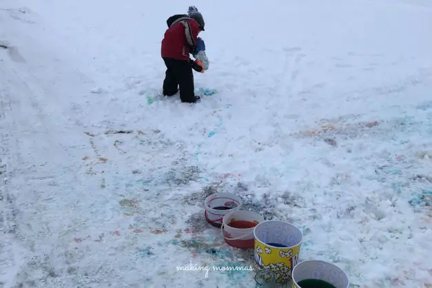 a boy spraying the snow with colored water out of a squirt gun