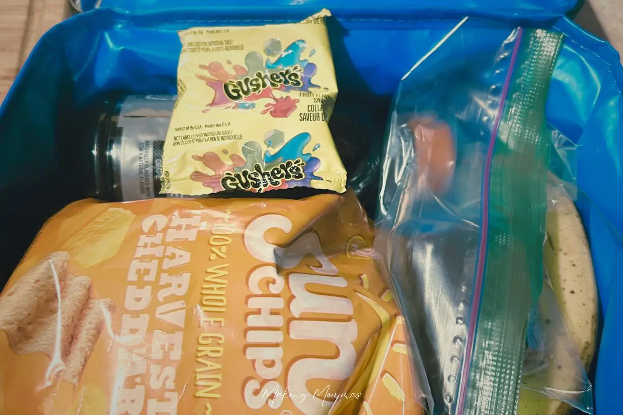 image of a school lunch box with chips, a banana, a ziplock baggies with a peanut butter bar, a gatorade and a fruit snacks