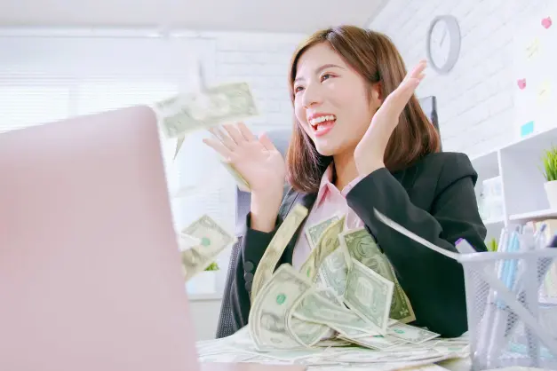 image of a woman surprised and happy sitting at a computer while money blows up around her