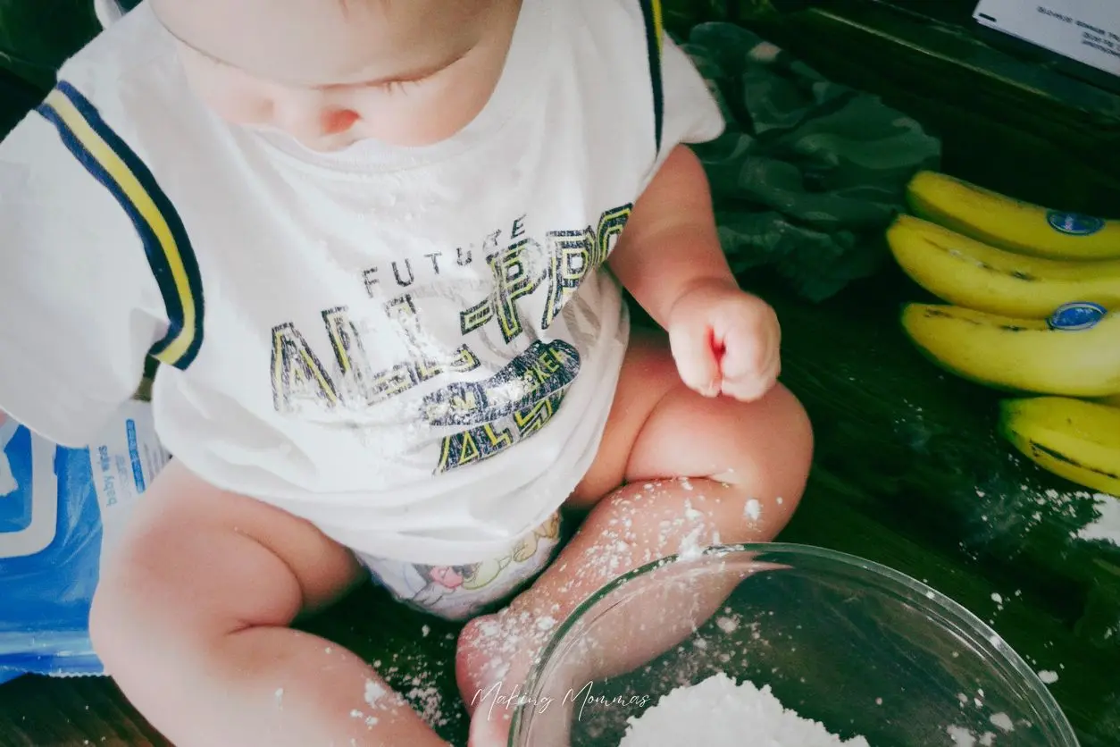 Image of a baby in a diaper and a t-shirt, playing with a bowl of powdered sugar