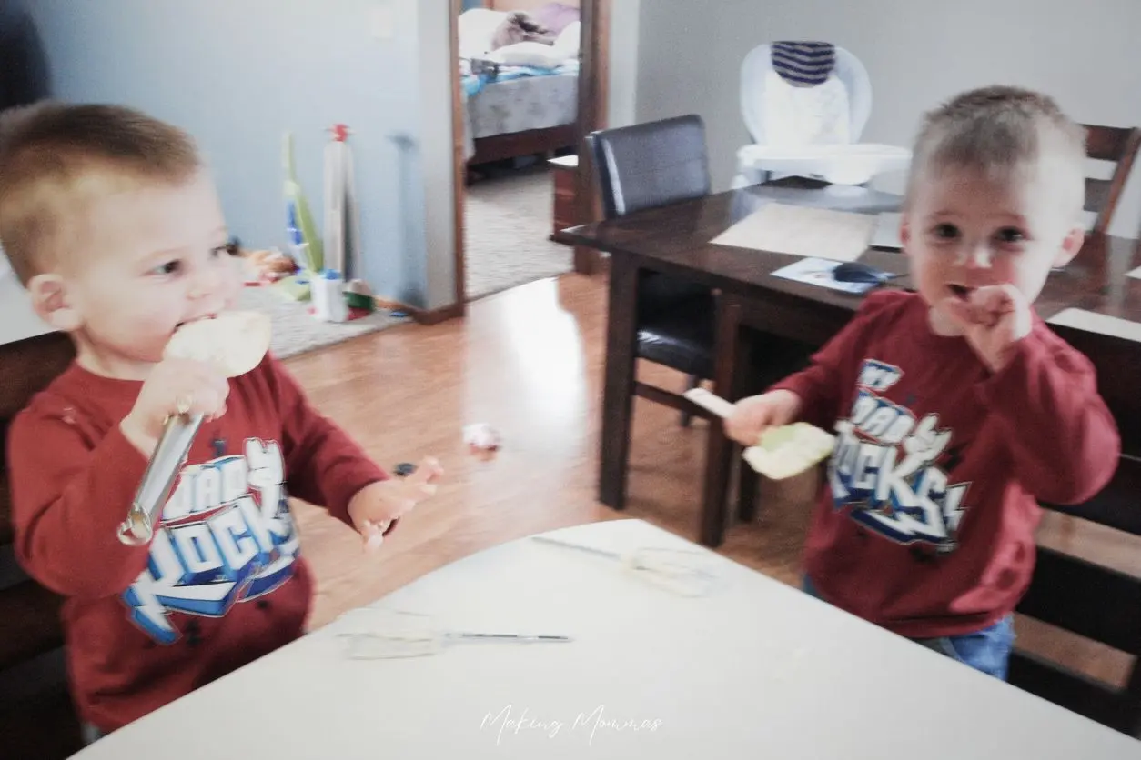 image of twin boys in red t-shirts that read "dad rocks", licking spatulas at the kitchen counter