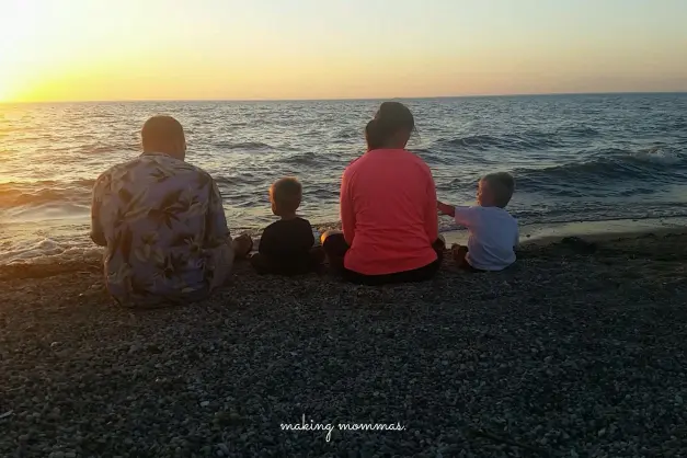 family sitting by lake shore as the sun sets