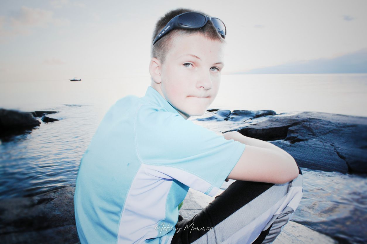 image of a boy with sunglasses on the top of his head sitting in front of a big body of water