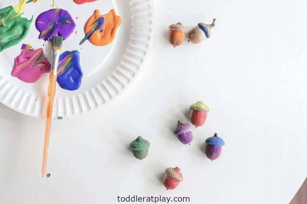 image of acorns painted in pastel colors with a paper plate full of paint