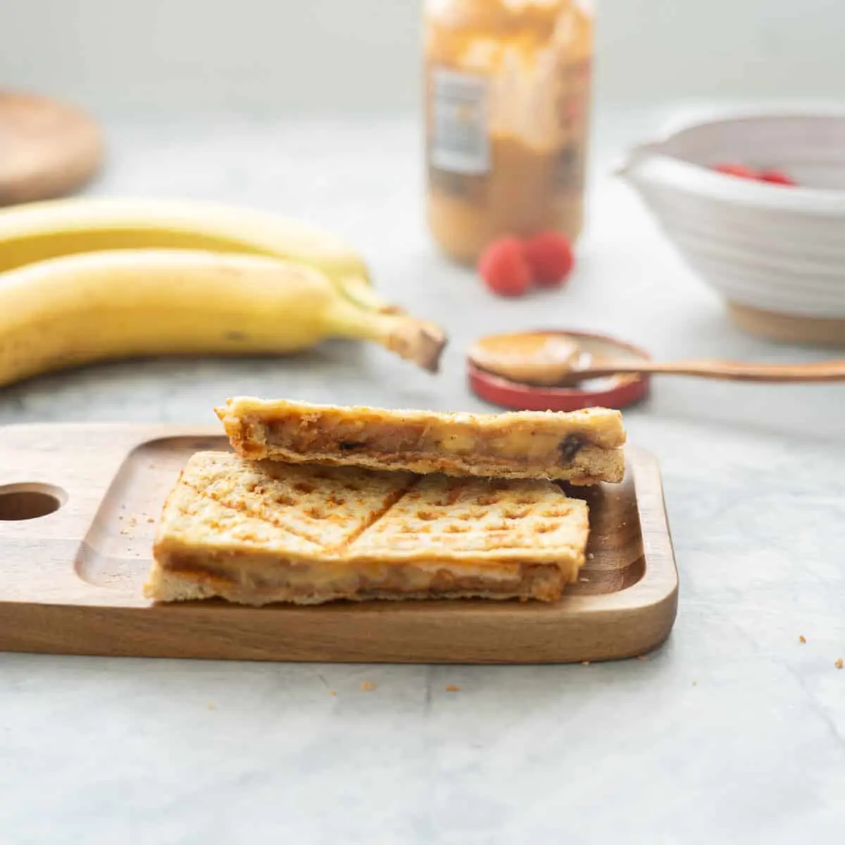 image of a peanut butter and banana sandwich on a plate with a banana in the background