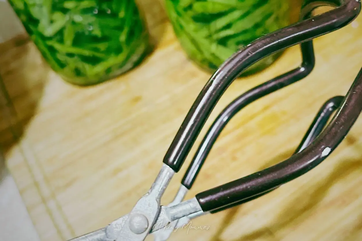 image of some tongs used to grab canning jars with green beans in the background