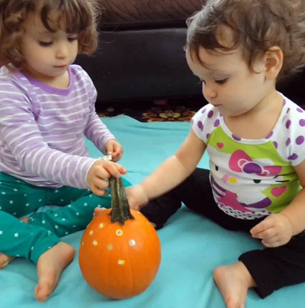 image of two toddler girls putting stickers on a pumpkin