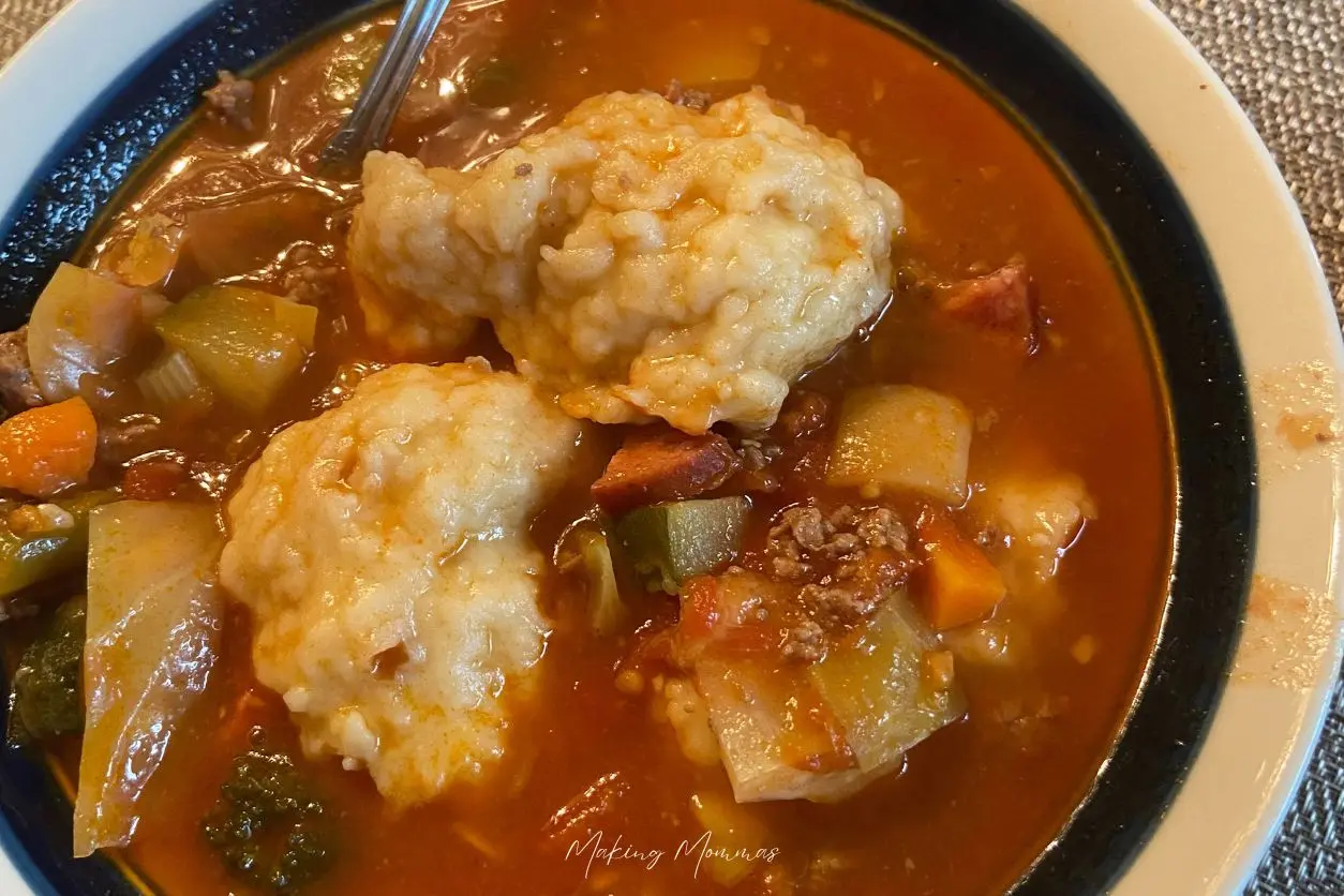 An image of hamburger veggie beef soup on a placemat with dumplings.