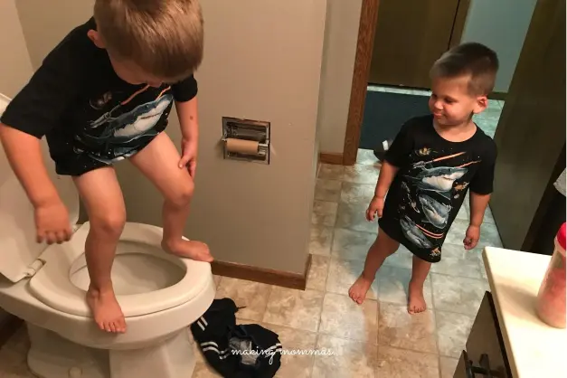 image of two boys playing in the bathroom, with one standing on the toilet