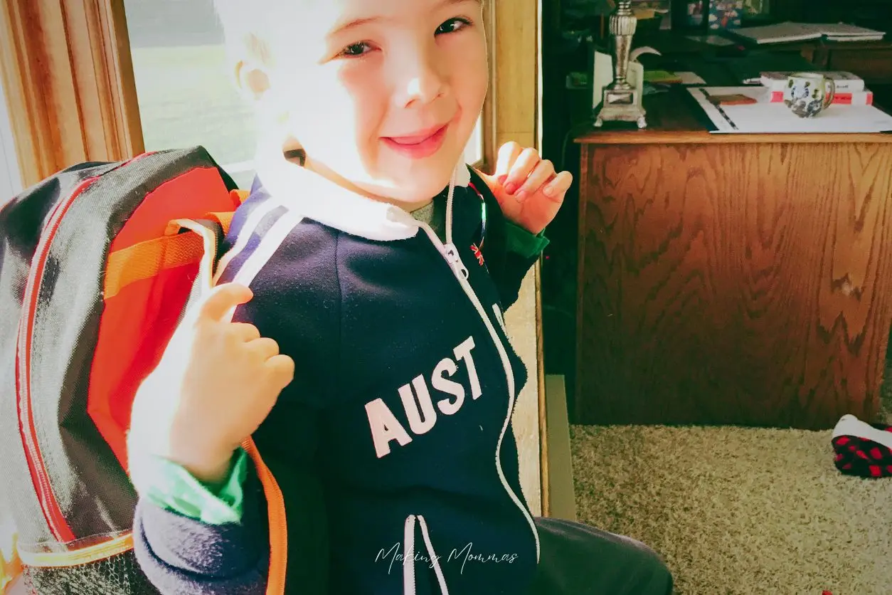 image of a little boy sitting by the window with his jacket and back pack on