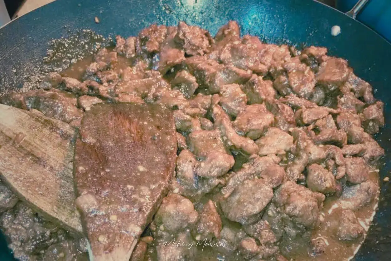 an image of venison simmering in a wok with sauce and two wooden spoons