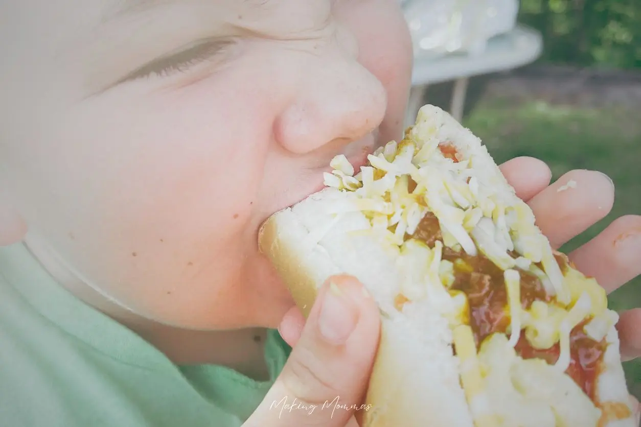 image of a boy taking a bite of a hot dog chopped with chili and mac and cheese