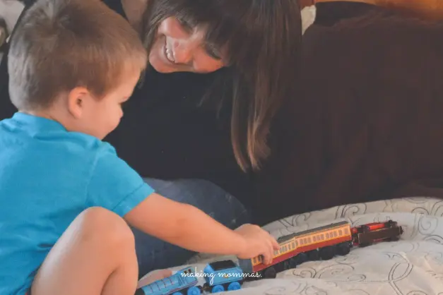 mom playing trains with son on bed