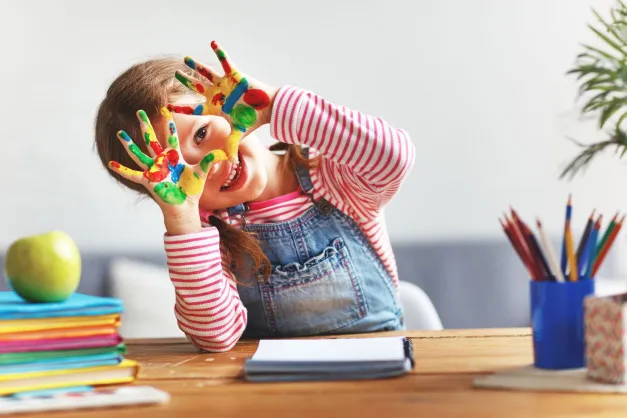 image of a girl in a preschool with colorful paint all over her palms