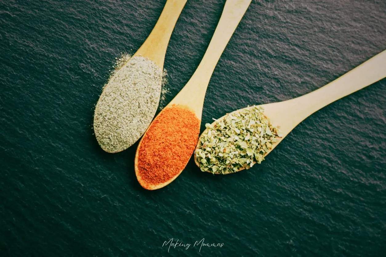 Image of spices laying in spoons on a black table.