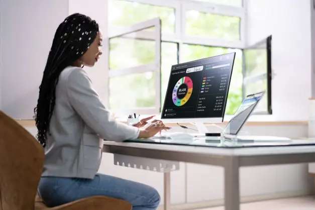 image of a woman sitting at a desk with a pie chart about expenses on the computer screen