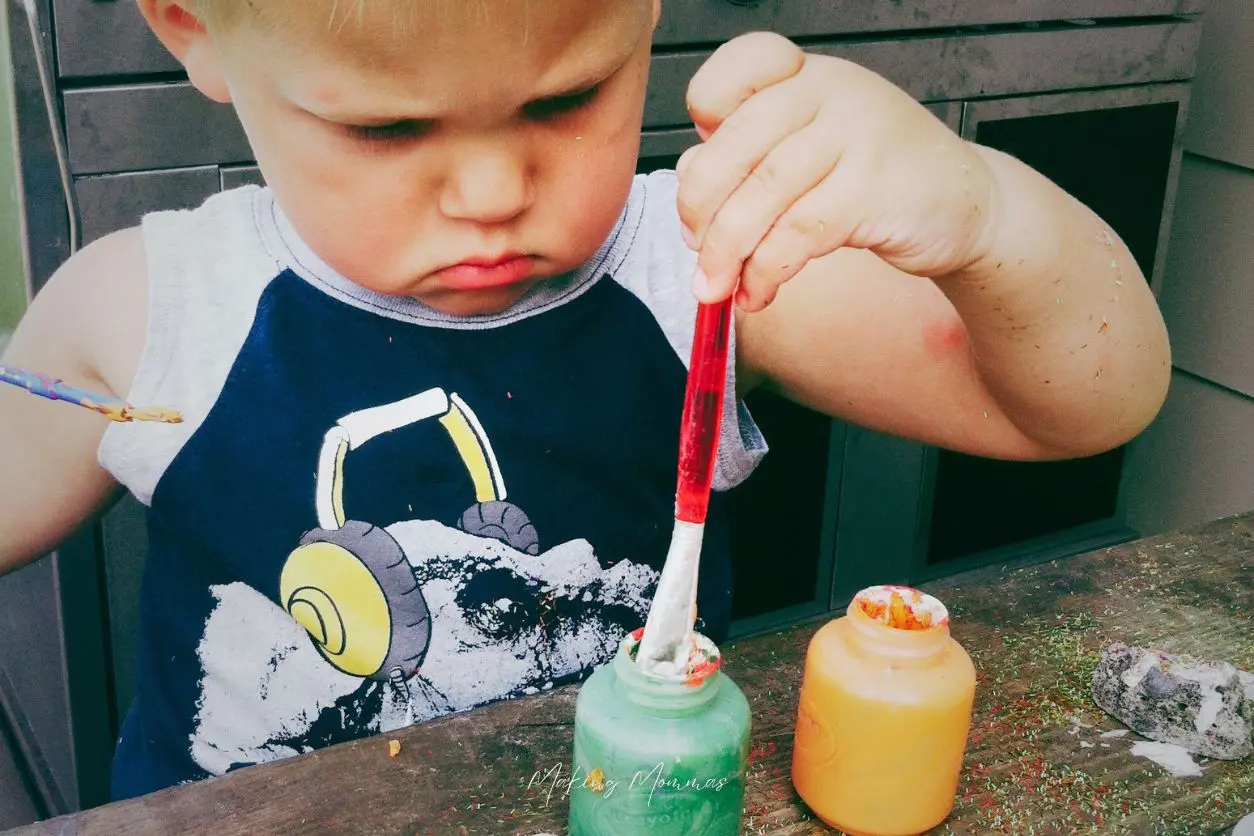 image of a little boy painting rocks and looking very frustrated
