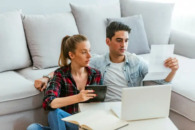 image of a couple sitting in front of a couch on the floor, budgeting