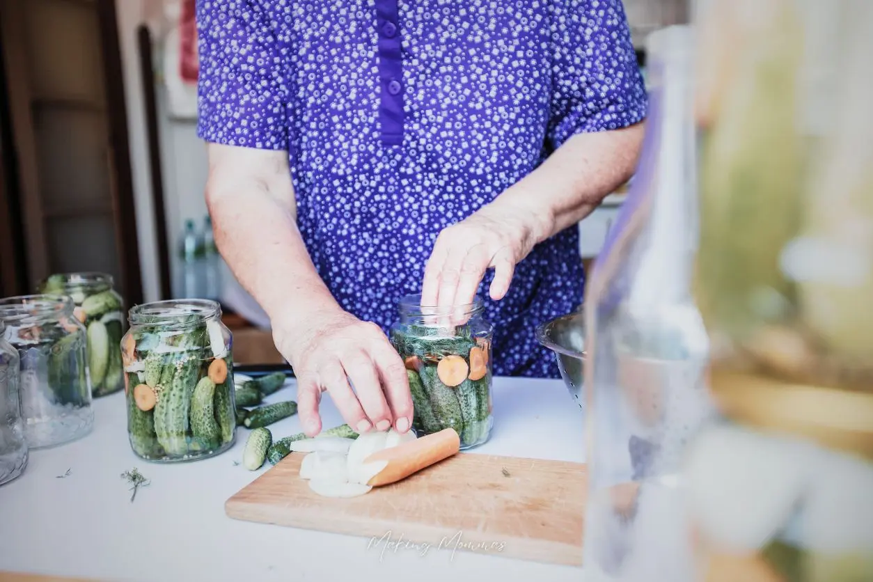 an image of a woman stuffing pickles, dill, and carrots into a jar