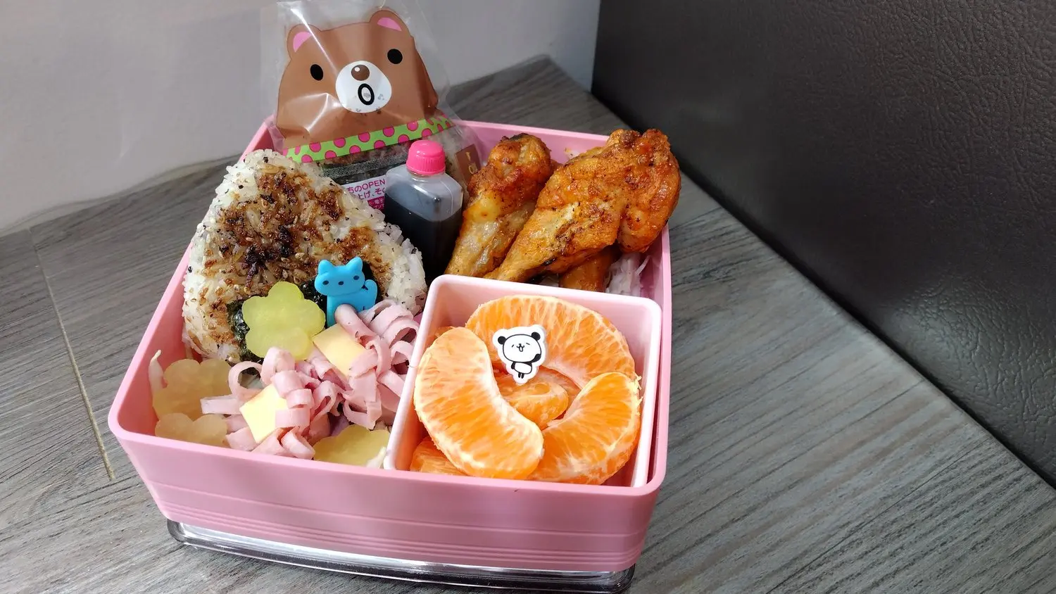 image of a bento box with chicken, a panda bear containers, oranges, and rice balls